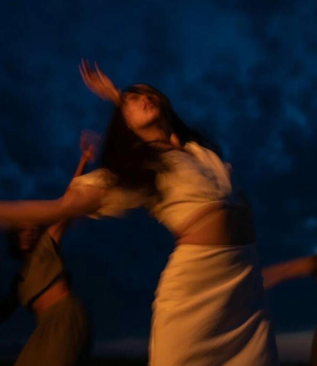 Blurred movement of a dancer expressing free-flowing motion at a 5Rhythms session under the night sky.